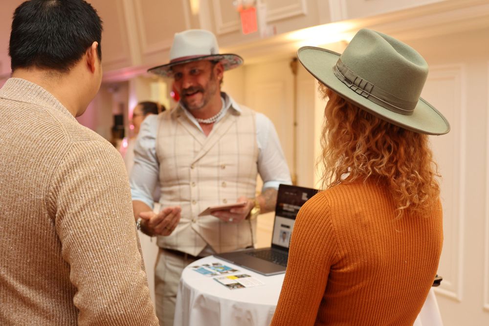 Event guests mingling at a vendor booth wearing stylish hats.