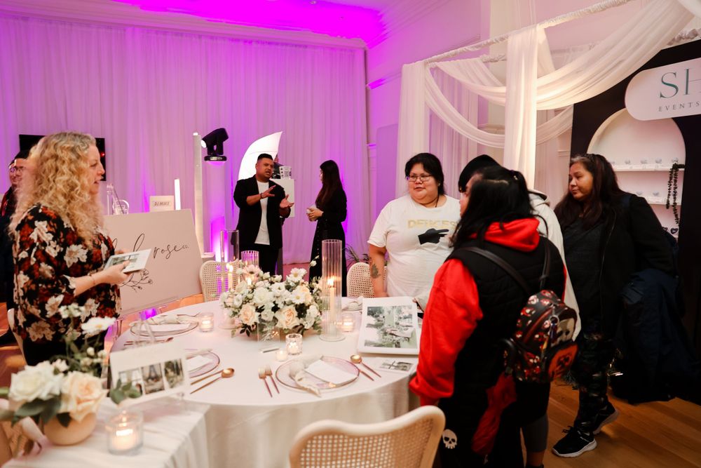 Wedding reception guests gathered around elegantly decorated tables with pink lighting and white decor.