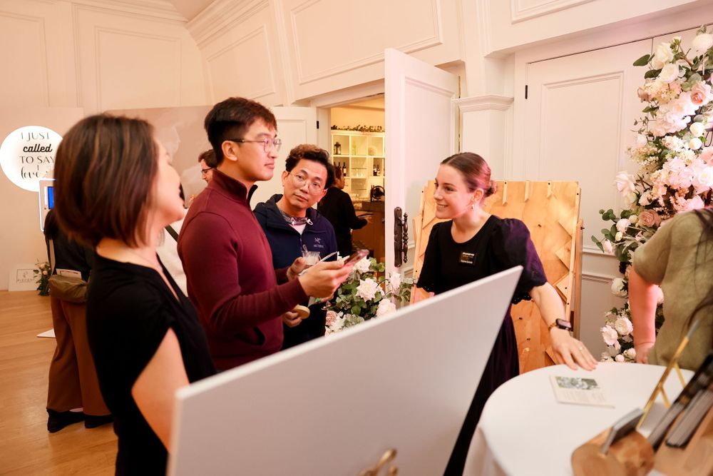 Group of people engaged in conversation around a display setup at an indoor event.