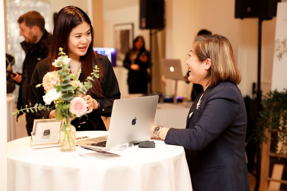 Two professionals having a discussion at an event table with flowers and laptops.
