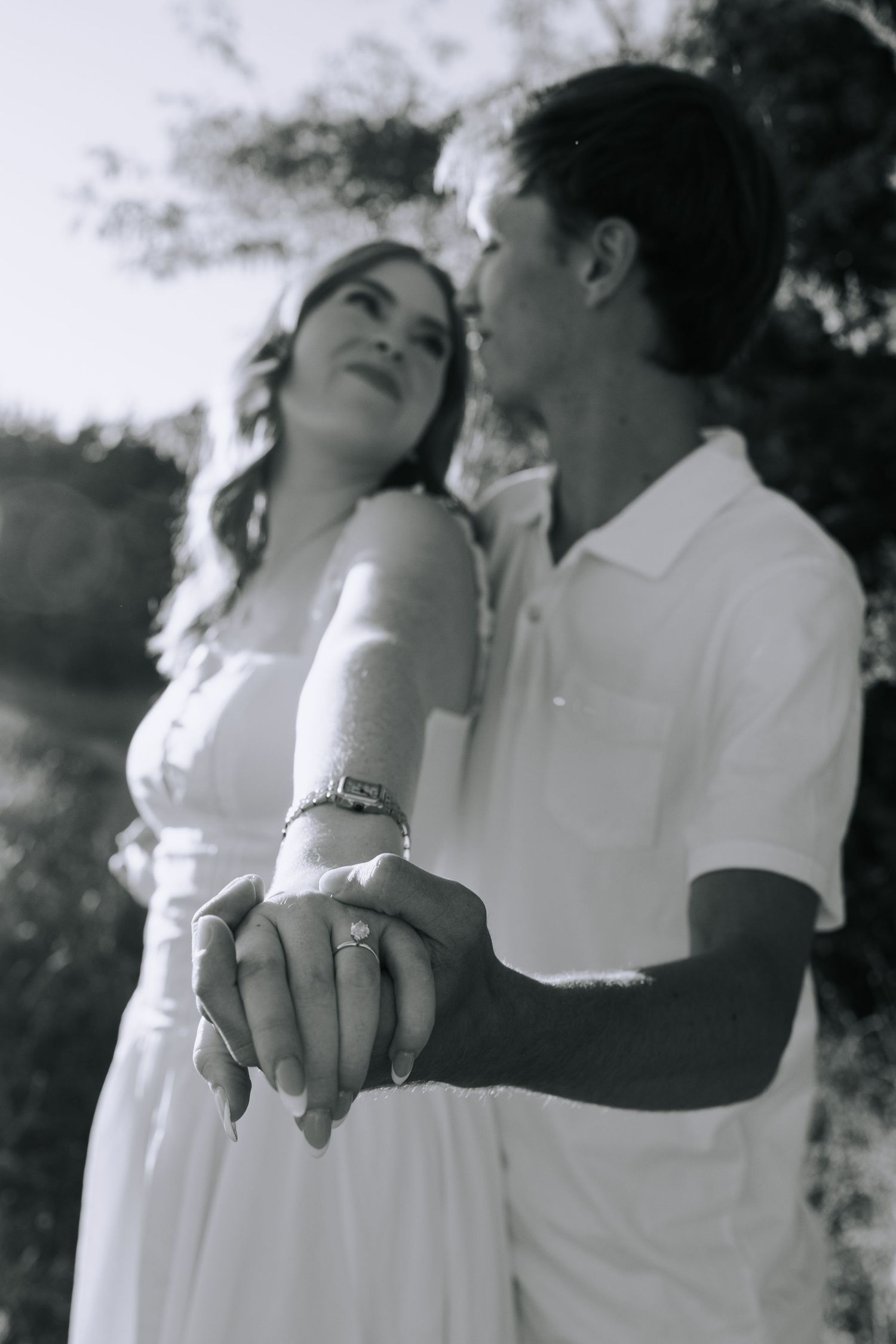 A couple holds hands while walking on a dirt path surrounded by trees.