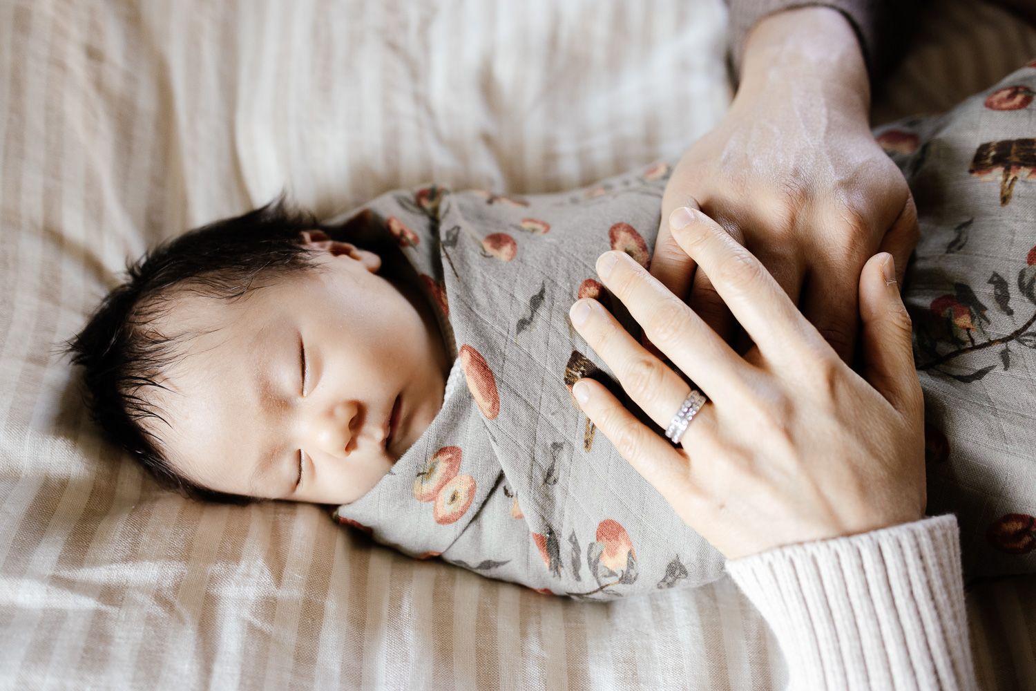 A swaddled baby sleeps while mom and dad put their hands on him