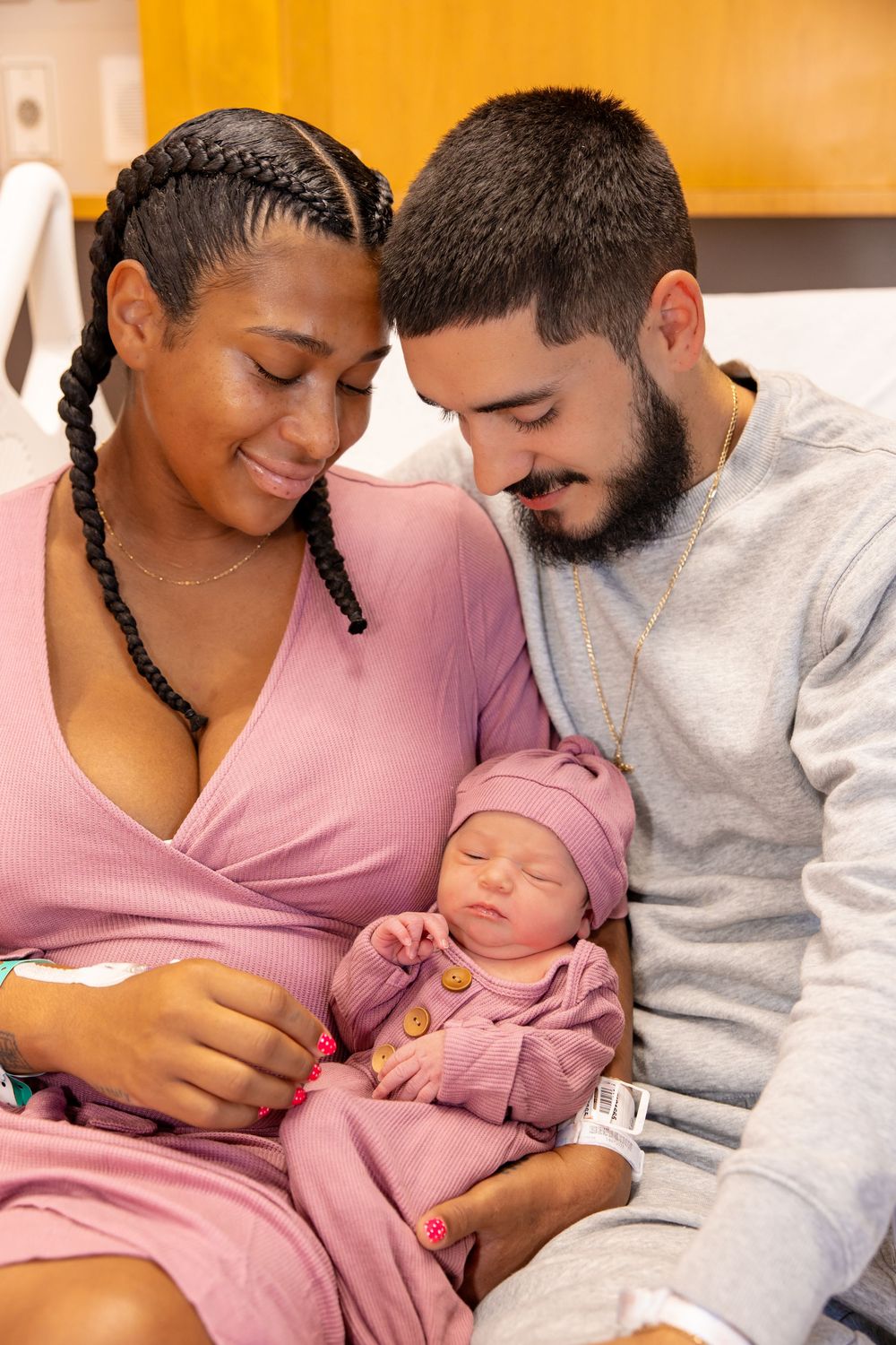 A couple in pink and gray clothing lovingly hold and gaze at their newborn baby in a series of tender moments.