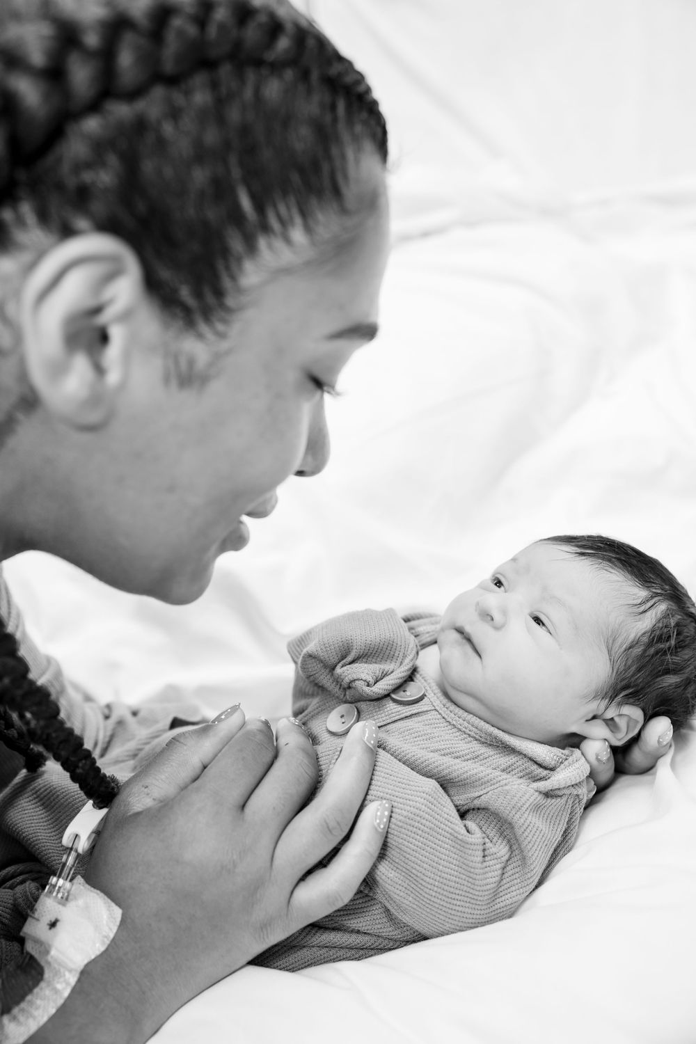 A tender black and white sequence showing a parent giving loving kisses to their baby on a white bed.