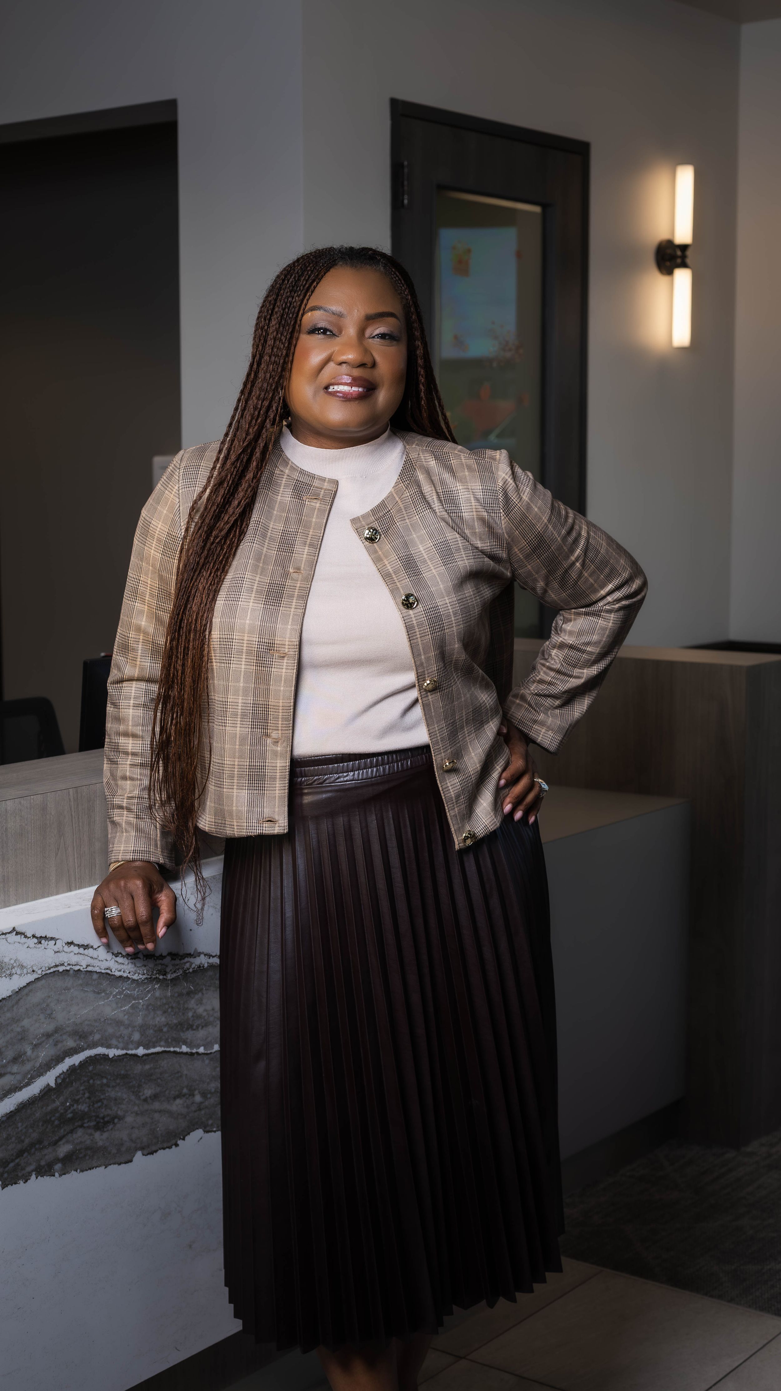 Professional portrait in modern office wearing plaid blazer and pleated skirt.