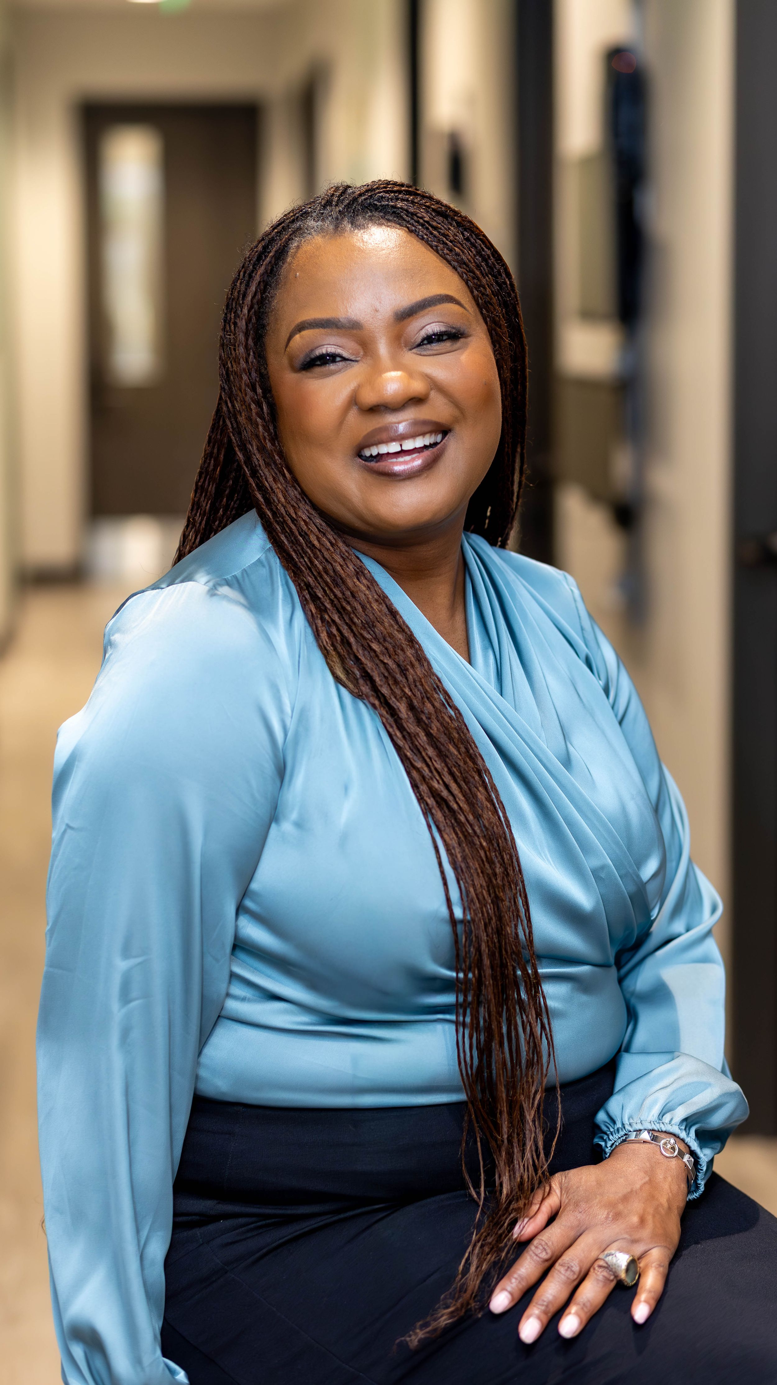 Healthcare professional in light blue blouse and navy skirt stands in office hallway.