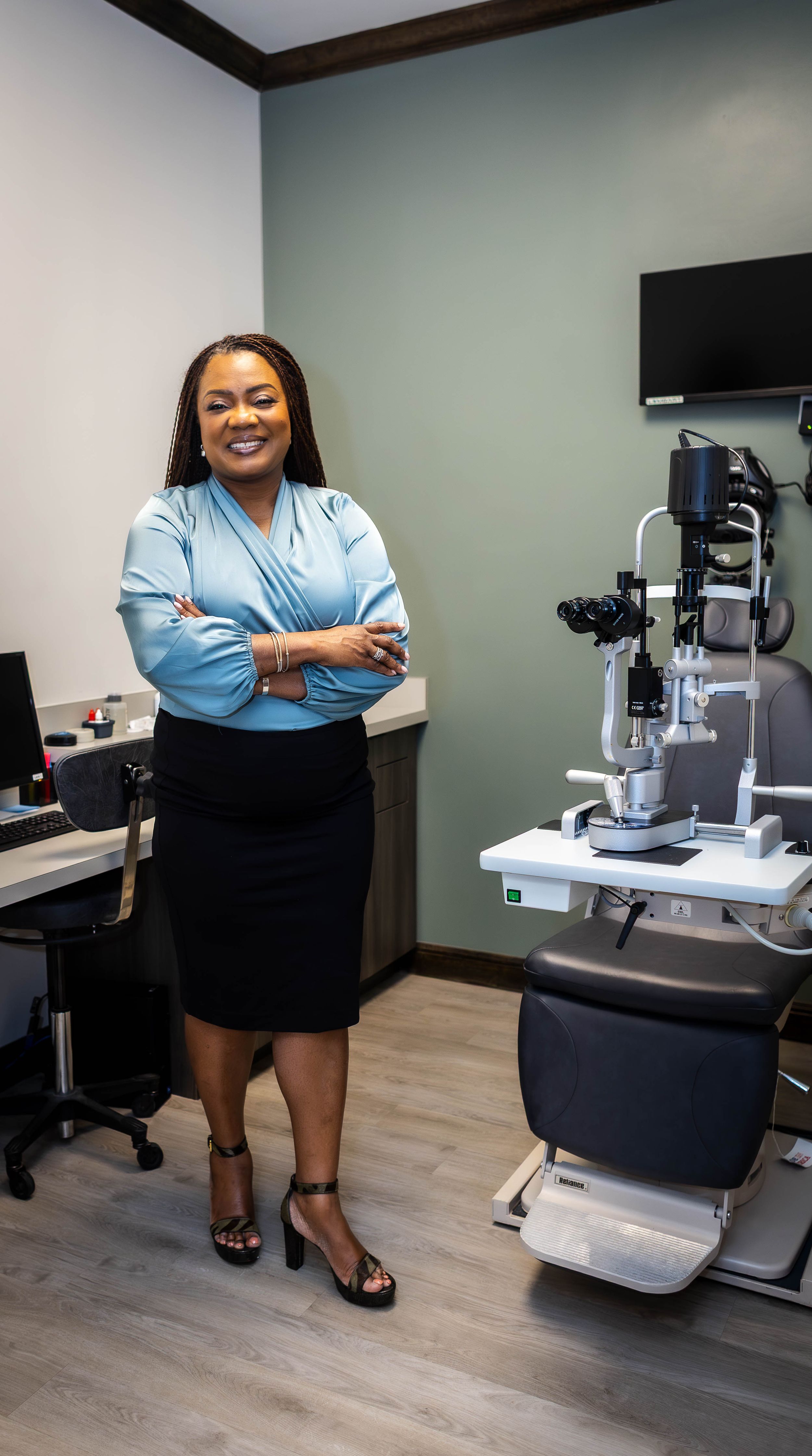 Medical professional in business attire poses in examination room with medical equipment.