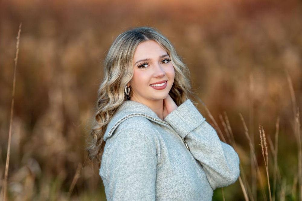 Blonde girl in gray hoodie sweater smiling in blurred autumn field background senior portrait.