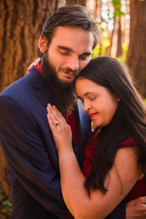 A romantic couple shares intimate moments in a forest setting with warm sunlight filtering through tall trees.
