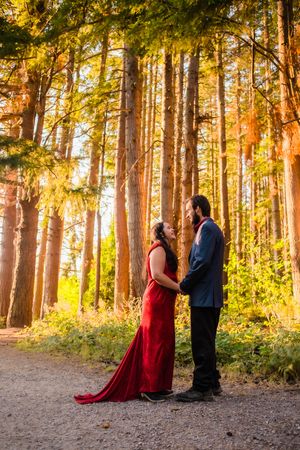 A couple in formal attire stands together in a sunlit forest during golden hour creating a romantic silhouette.