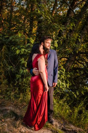 A couple embraces in a romantic outdoor setting with golden sunlight filtering through autumn foliage in the background.