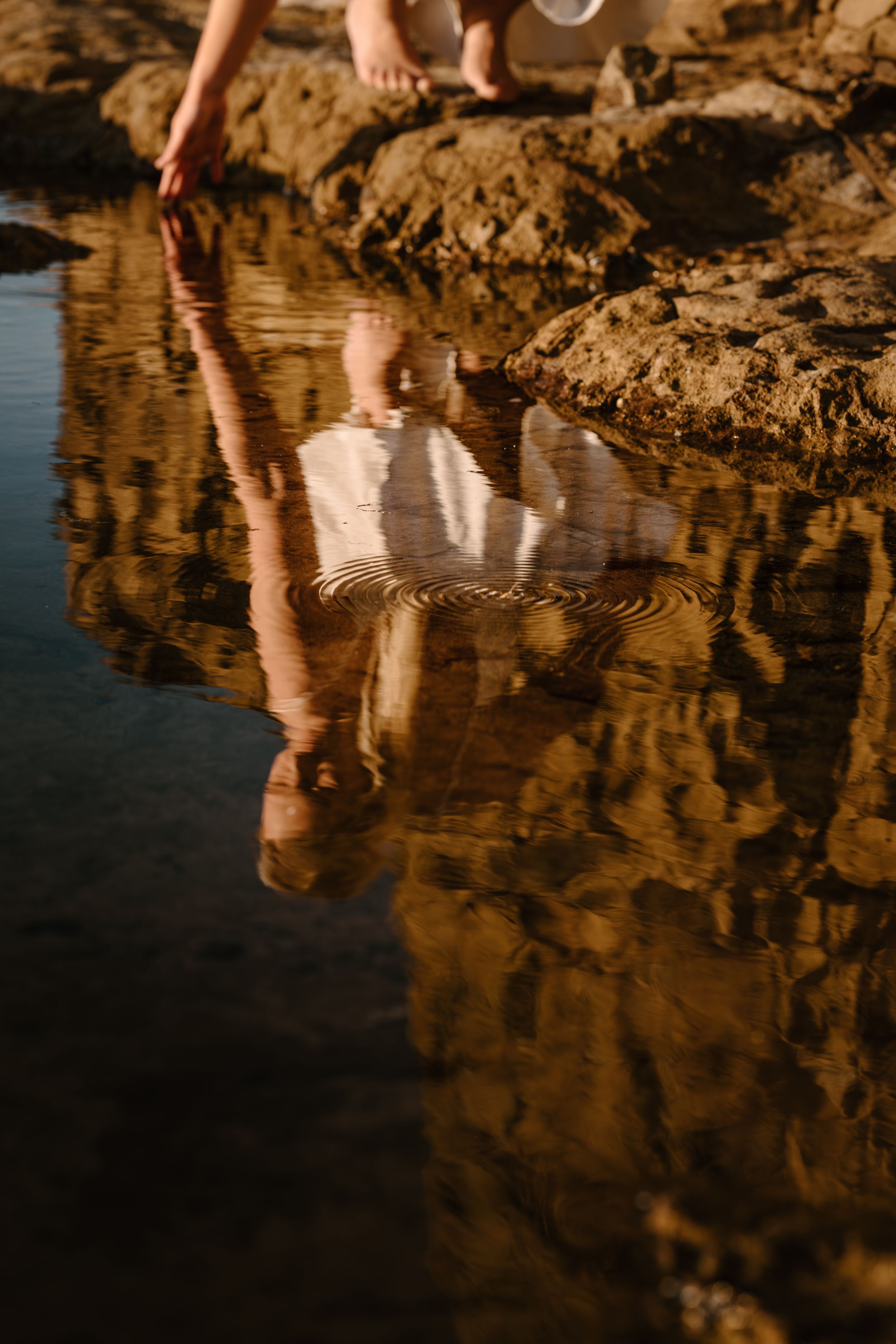 Rippling reflections in shallow water create golden patterns against rocky terrain at sunset.