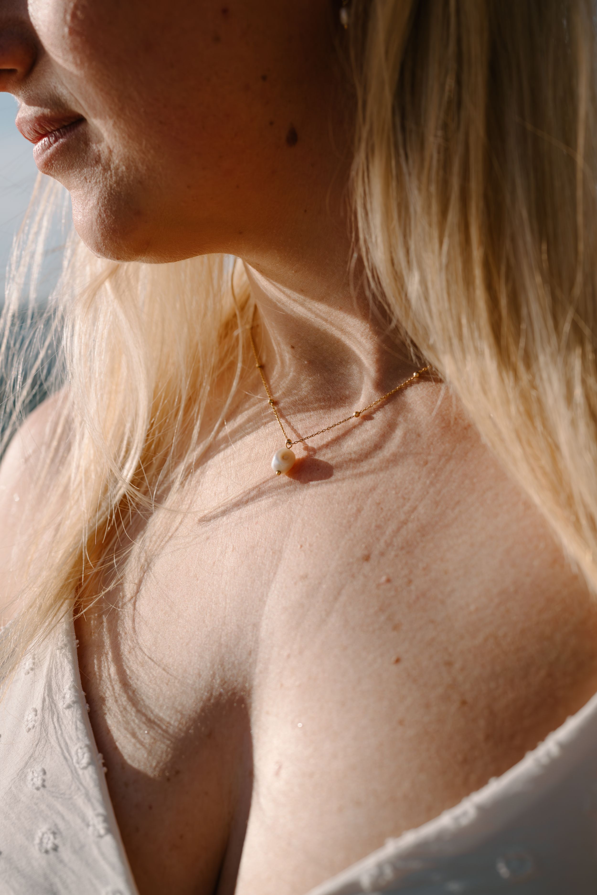 Close-up portrait of blonde hair and delicate necklace in soft natural lighting.
