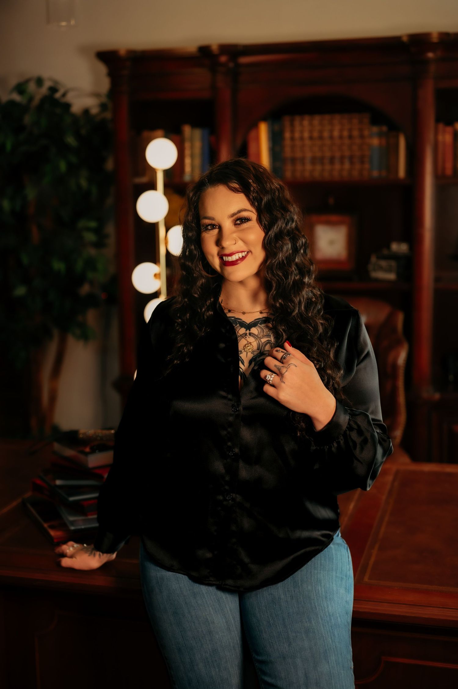 Indoor portrait with warm lighting and vintage decor featuring someone in a black top and jeans.