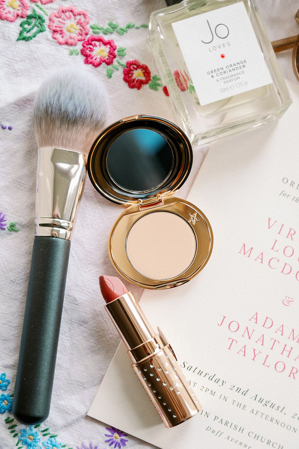 Wedding invitation and makeup products styled with floral accents on white background.