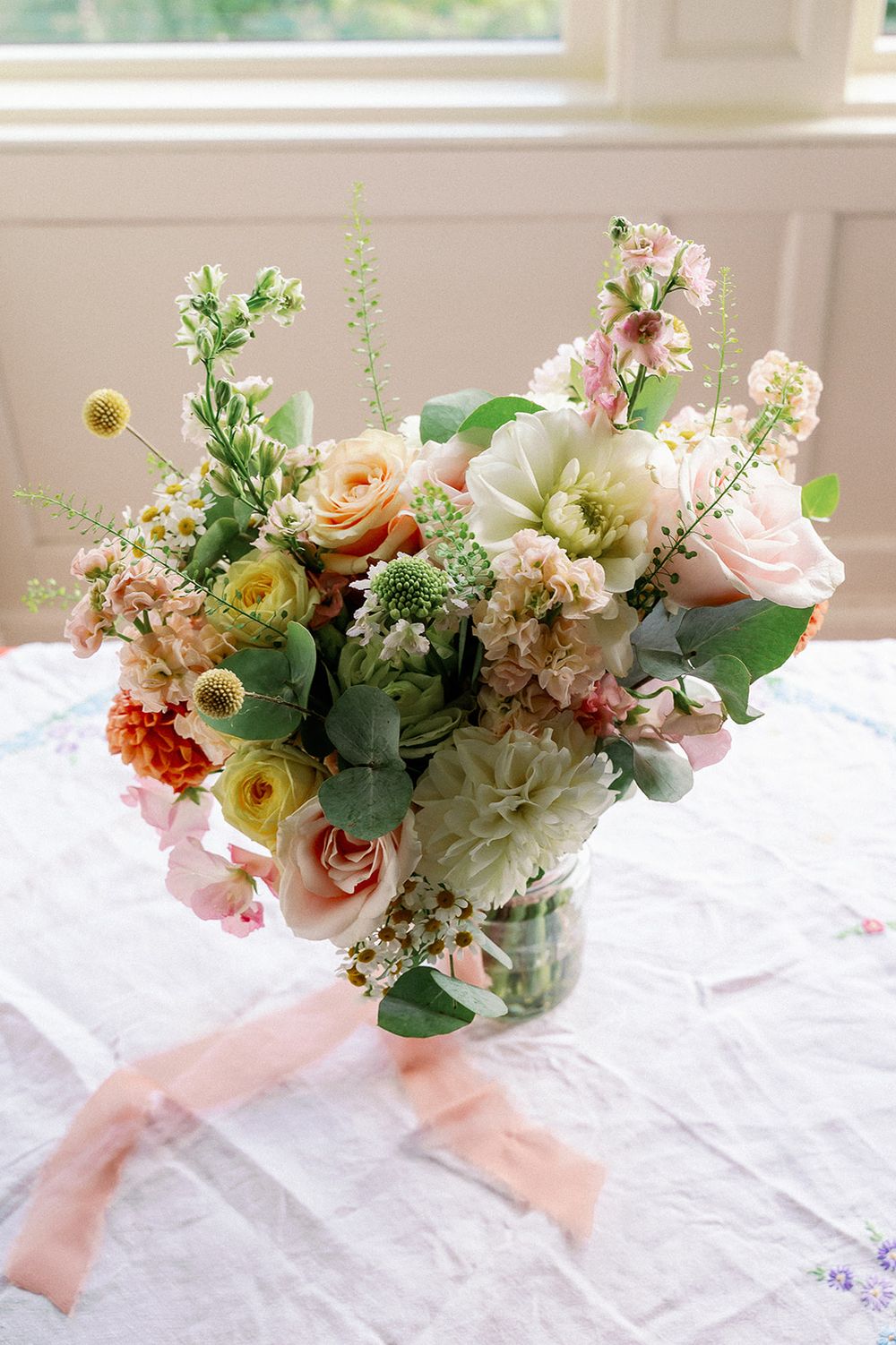 Romantic pastel floral centerpieces with roses and greenery arranged on white tablecloths.