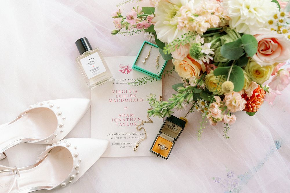 Wedding day details including perfume bottles and floral arrangements on white surface.