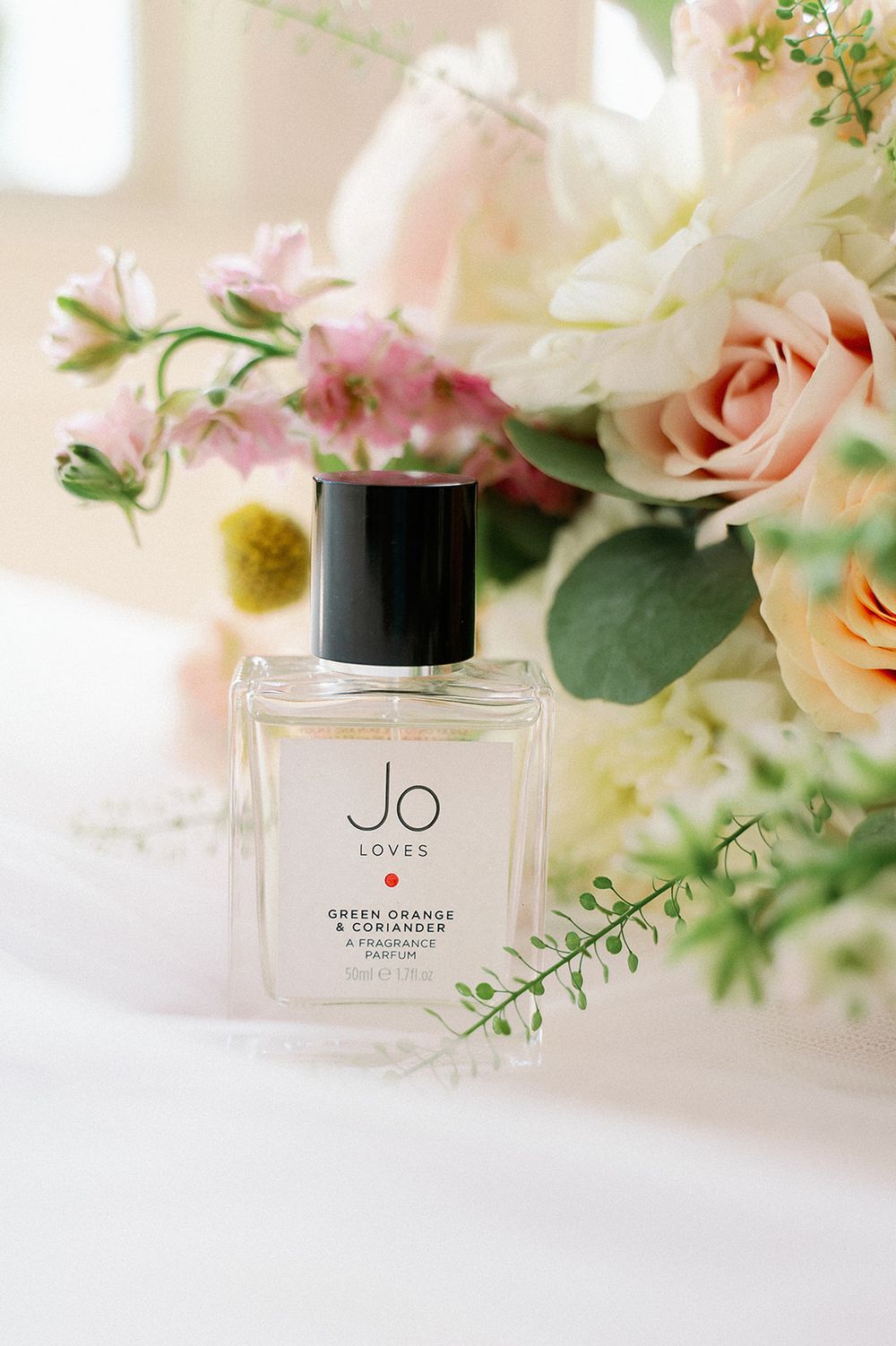 Elegant perfume bottles and wedding accessories styled with soft pink roses and greenery.
