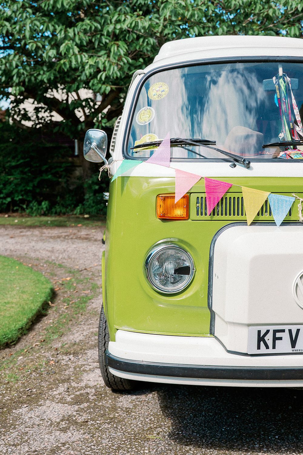 Front view of a vintage green and white Volkswagen van decorated with colorful bunting.