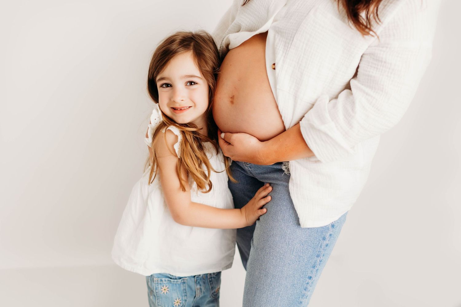 Intimate maternity photo series showing tender moments between expecting parents against a white backdrop.