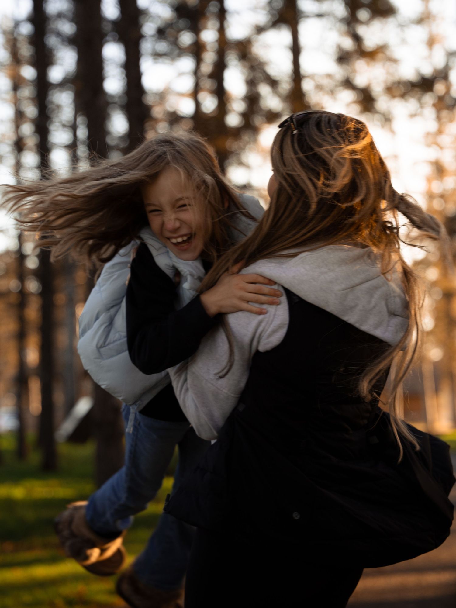 Two people playing and laughing together in a forest during golden hour.