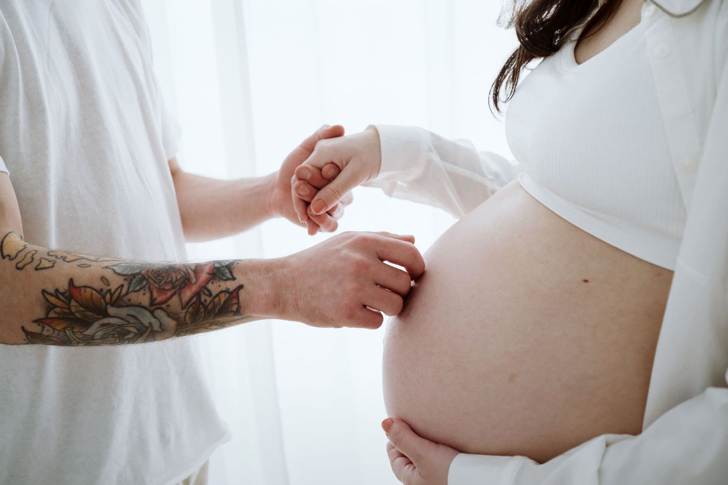 A pregnant woman in a white shirt poses against a light background during a maternity photoshoot.
