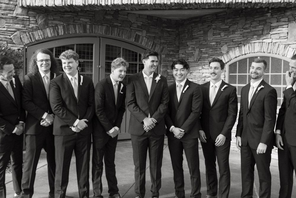 Groomsmen in dark suits stand in a row at a formal wedding ceremony.