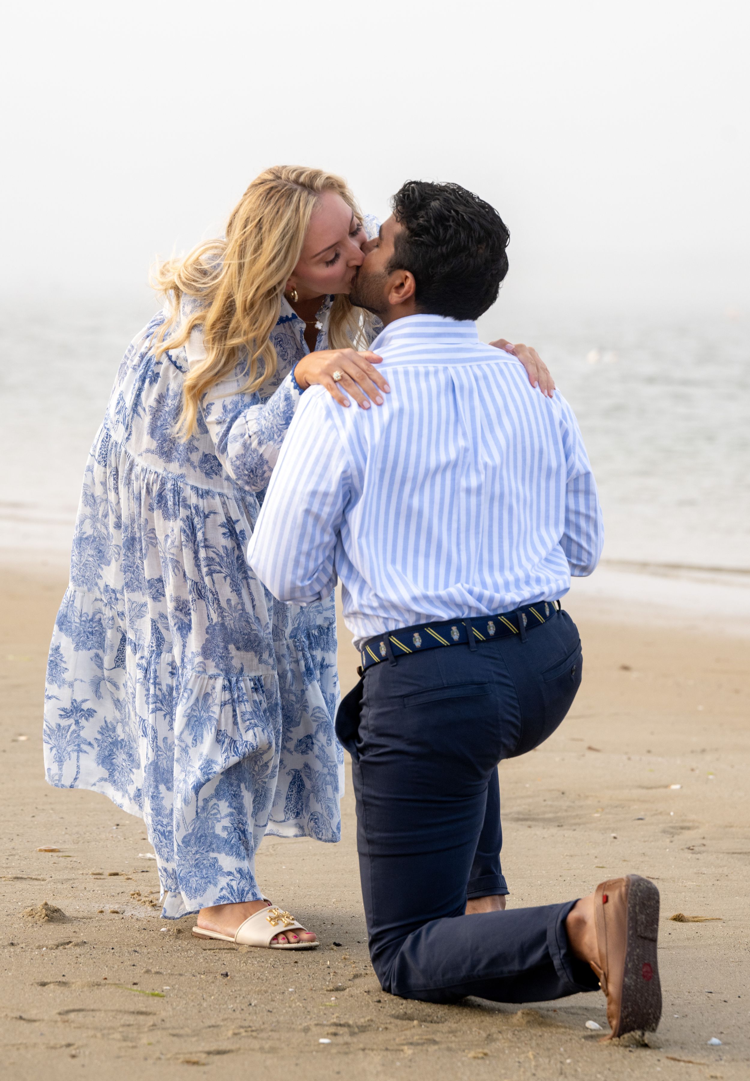 A romantic beach proposal scene with a couple in blue and white attire sharing a special moment on the sand.