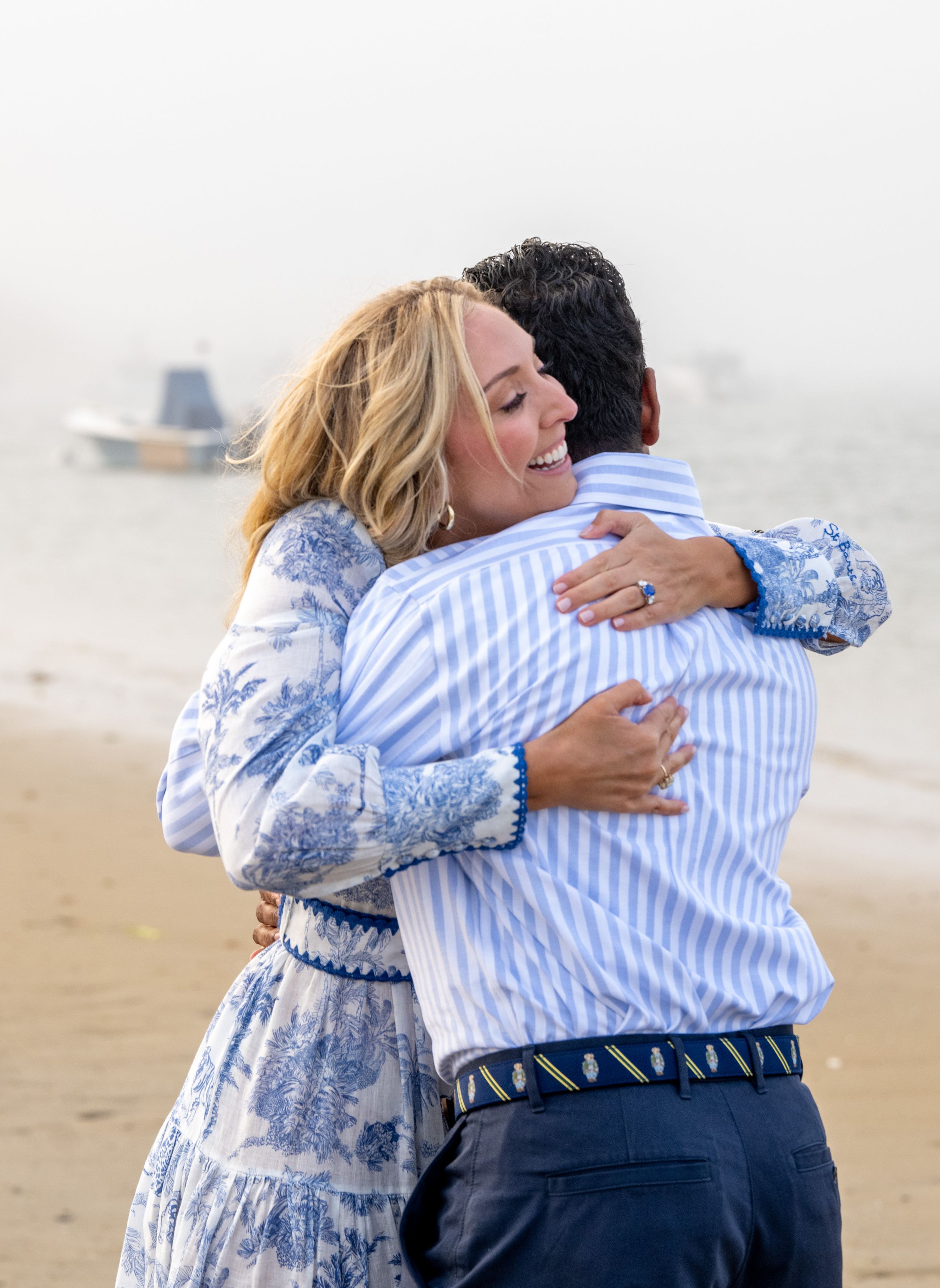 Two people share an emotional embrace on a beach during a special moment.