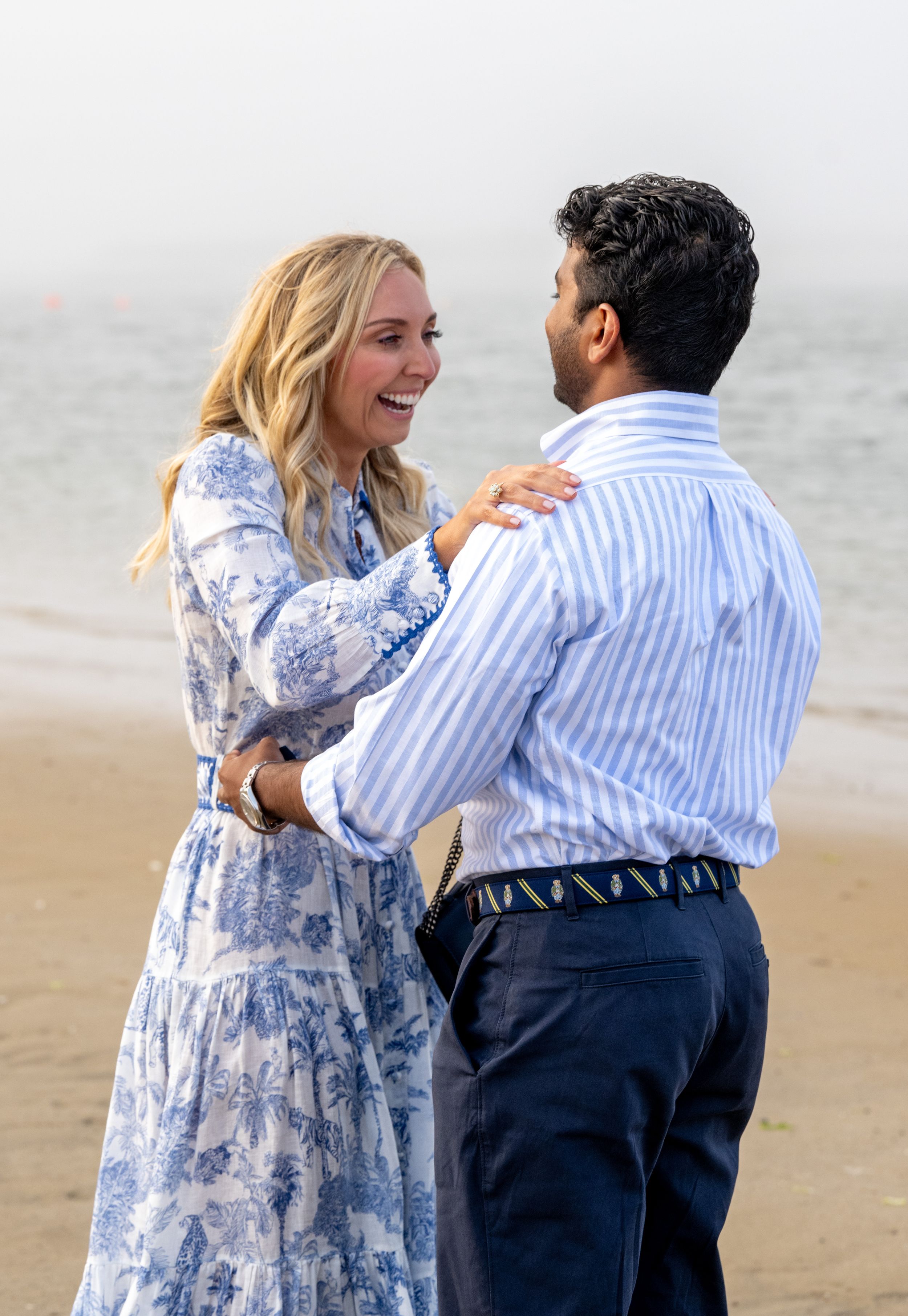 A joyful celebration moment between two people on a beach with the ocean in view.