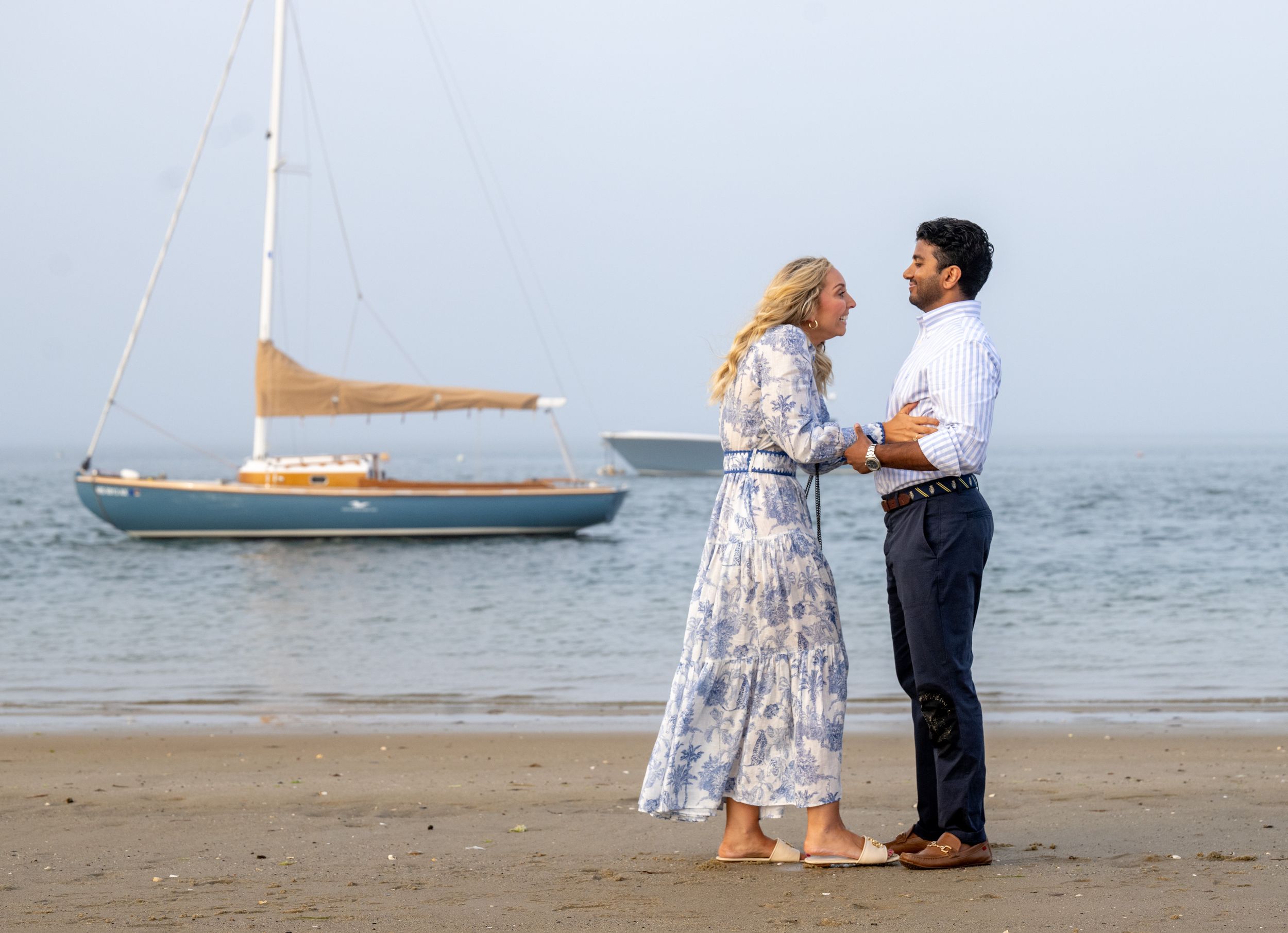 A romantic beach scene with sailboats in the distance as a couple shares a special moment.
