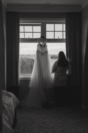 A wedding dress hangs in a window while someone gazes out at the view.