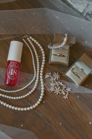 Wedding accessories including pearl necklaces, rings, and nail polish arranged on a wooden surface.