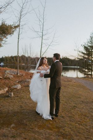 Couple dances together on a hillside overlooking a serene lake at sunset.