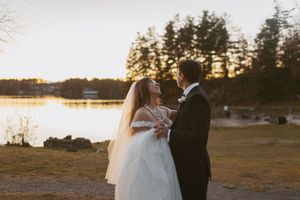 Wedding couple poses against the backdrop of a sunset-lit lake and autumn trees.