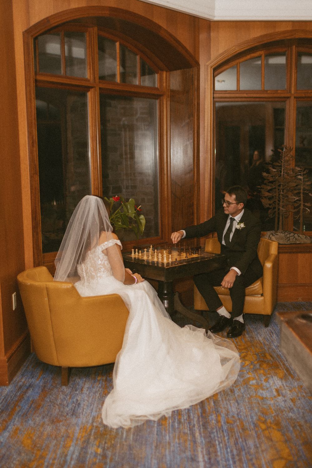A bride in a flowing white dress twirls gracefully on a hardwood floor in an elegant room with arched windows.