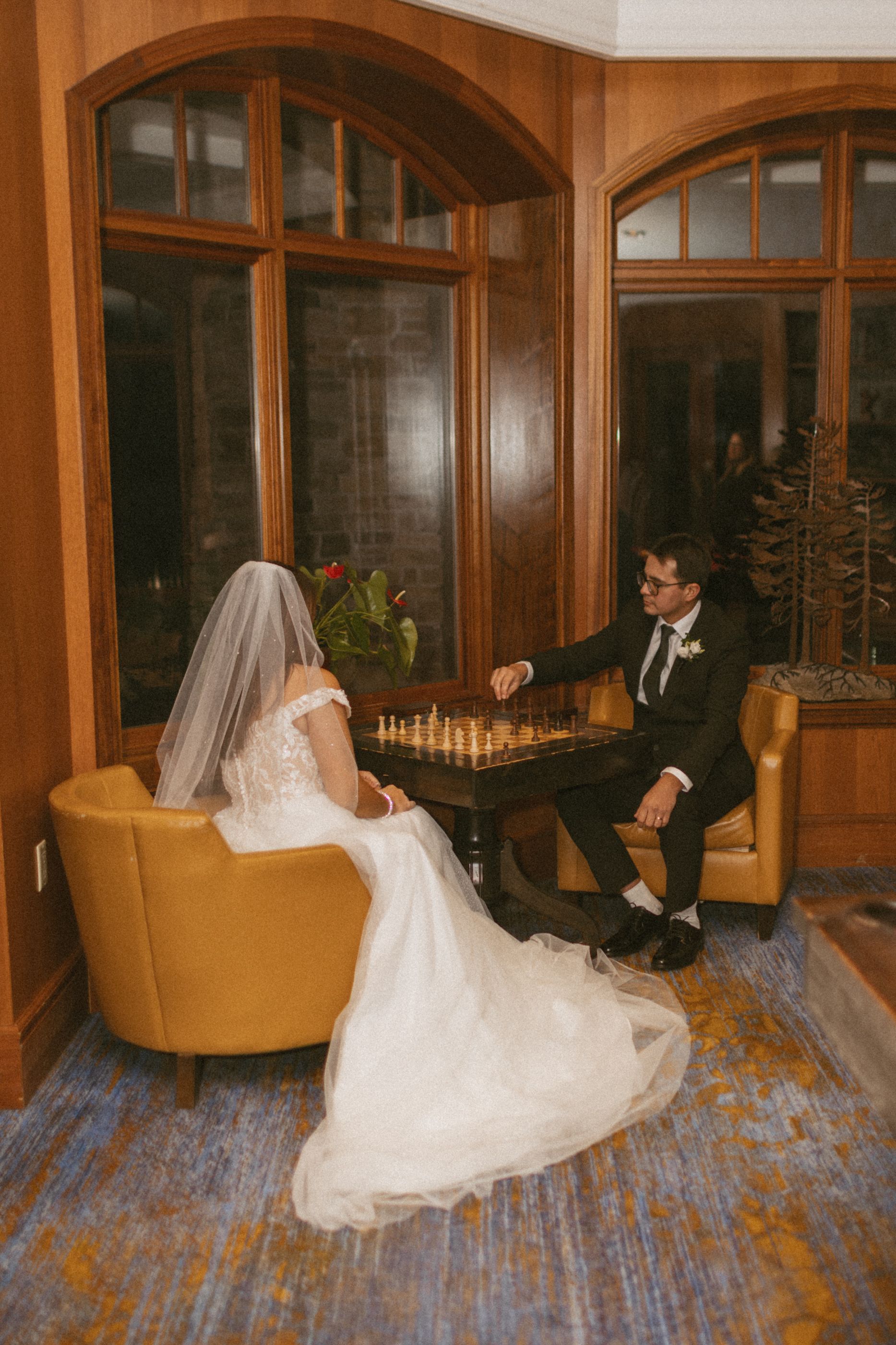A bride in a flowing white dress twirls gracefully on a hardwood floor in an elegant room with arched windows.