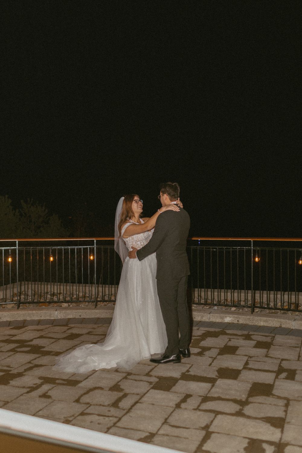 A couple shares an intimate dance moment on a stone patio at night under soft lighting.