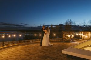 A romantic nighttime wedding scene on a terrace with string lights and a dramatic blue sky backdrop.