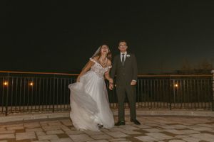 A couple dances together on an outdoor terrace under evening lights with a scenic view.