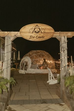 An illuminated outdoor wedding venue with a wooden Tea Caves sign and geodesic dome structure.