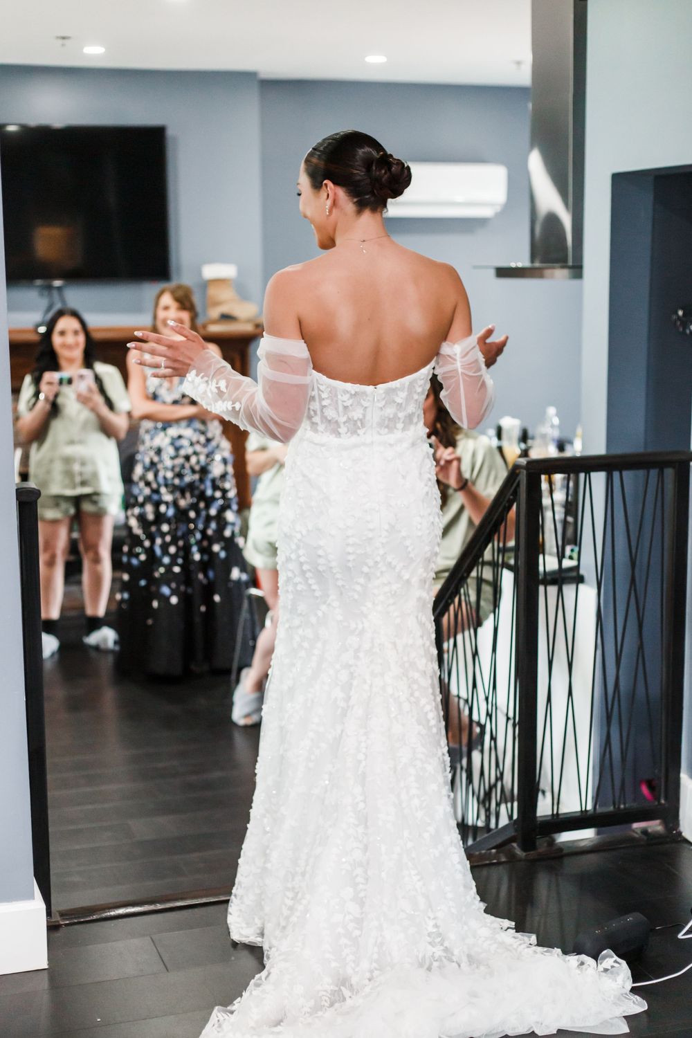 Bride in a white lace dress looks at herself in a mirrored room during a wedding dress fitting.