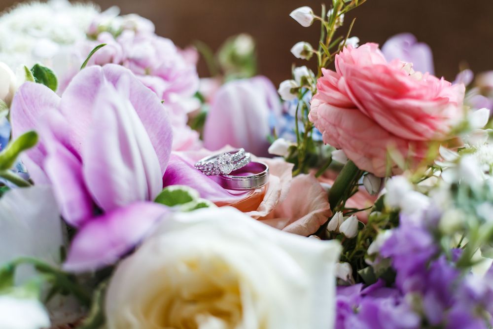 Wedding rings nestled among pink and purple roses in a romantic floral arrangement.