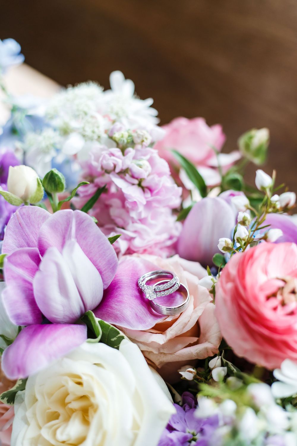 Wedding rings nestled among pink, purple and white flowers in a delicate floral arrangement.