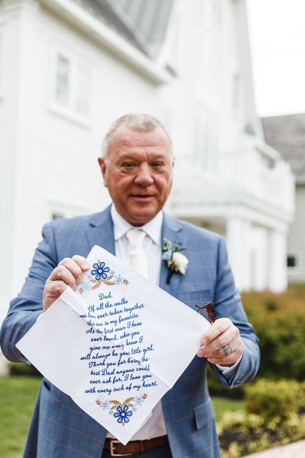 Person in blue suit holding up an embroidered handkerchief with written message.