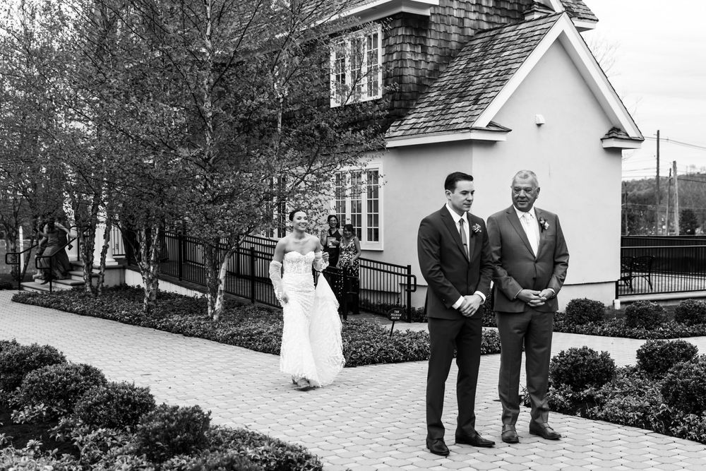 Wedding party members gather outside a classic white house with black and white photography.