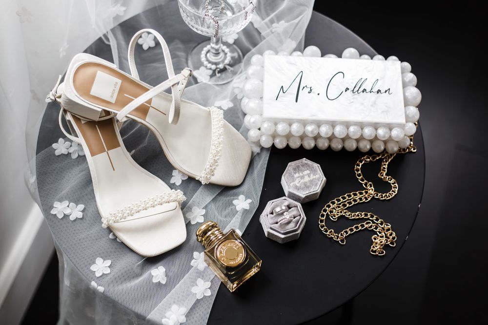 Wedding accessories including jewelry, shoes, and decorative items arranged on reflective surface.