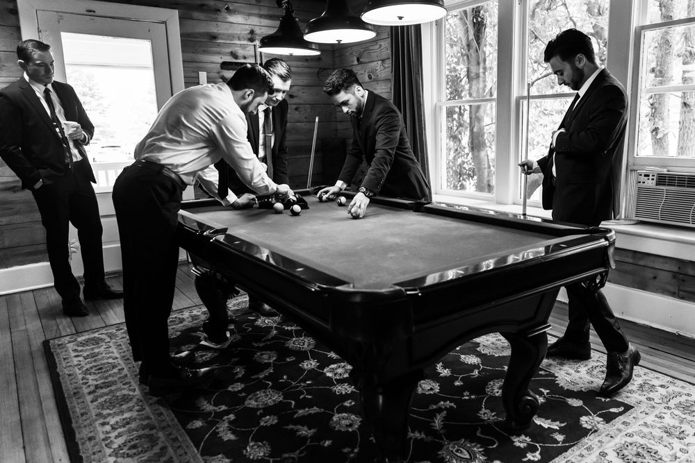 Wedding party members playing pool in a rustic indoor setting.