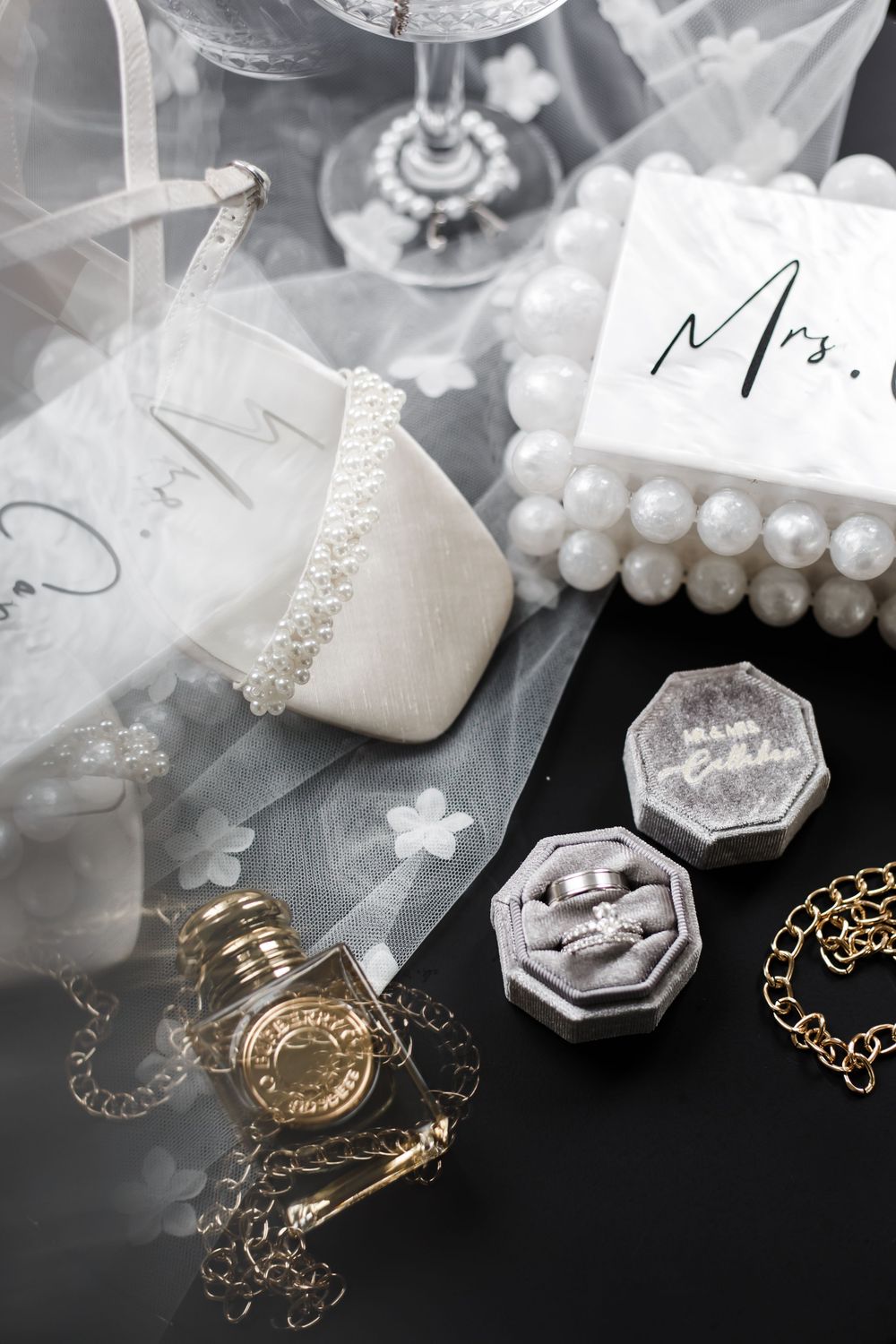 Wedding accessories including pearl bracelets, vintage perfume bottles, and delicate jewelry on a dark surface.