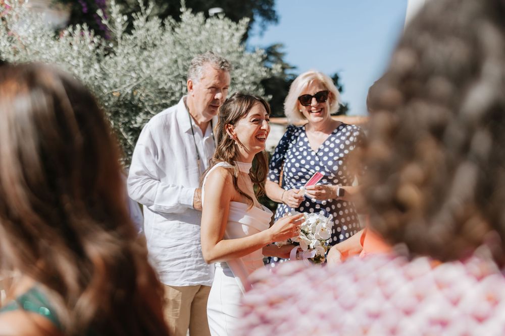 Guests celebrate at an outdoor wedding ceremony with pink confetti petals falling in the sunlight.